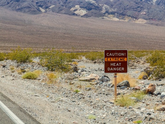 A sign on the side of a desert road reads, "Caution! Extreme Heat Danger"