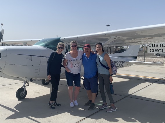 Four people pose in front of a small plane out on the tarmac.