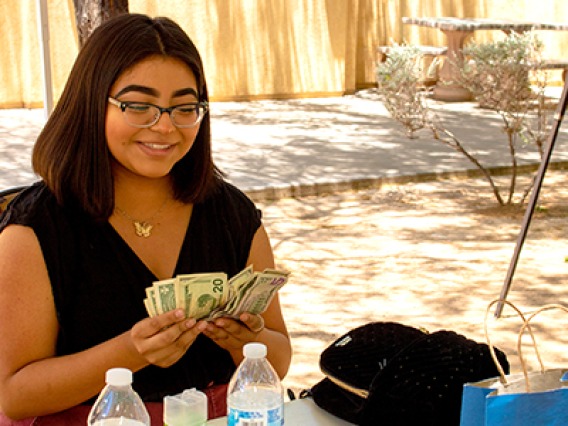 A young woman counts cash and smiles after participating in a 2019 NAYEP market event.