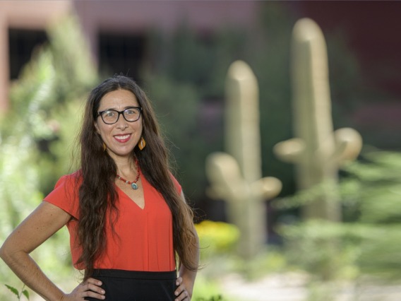 Stephanie Russo Carroll poses in front of saguaro cactus in a red shirt.