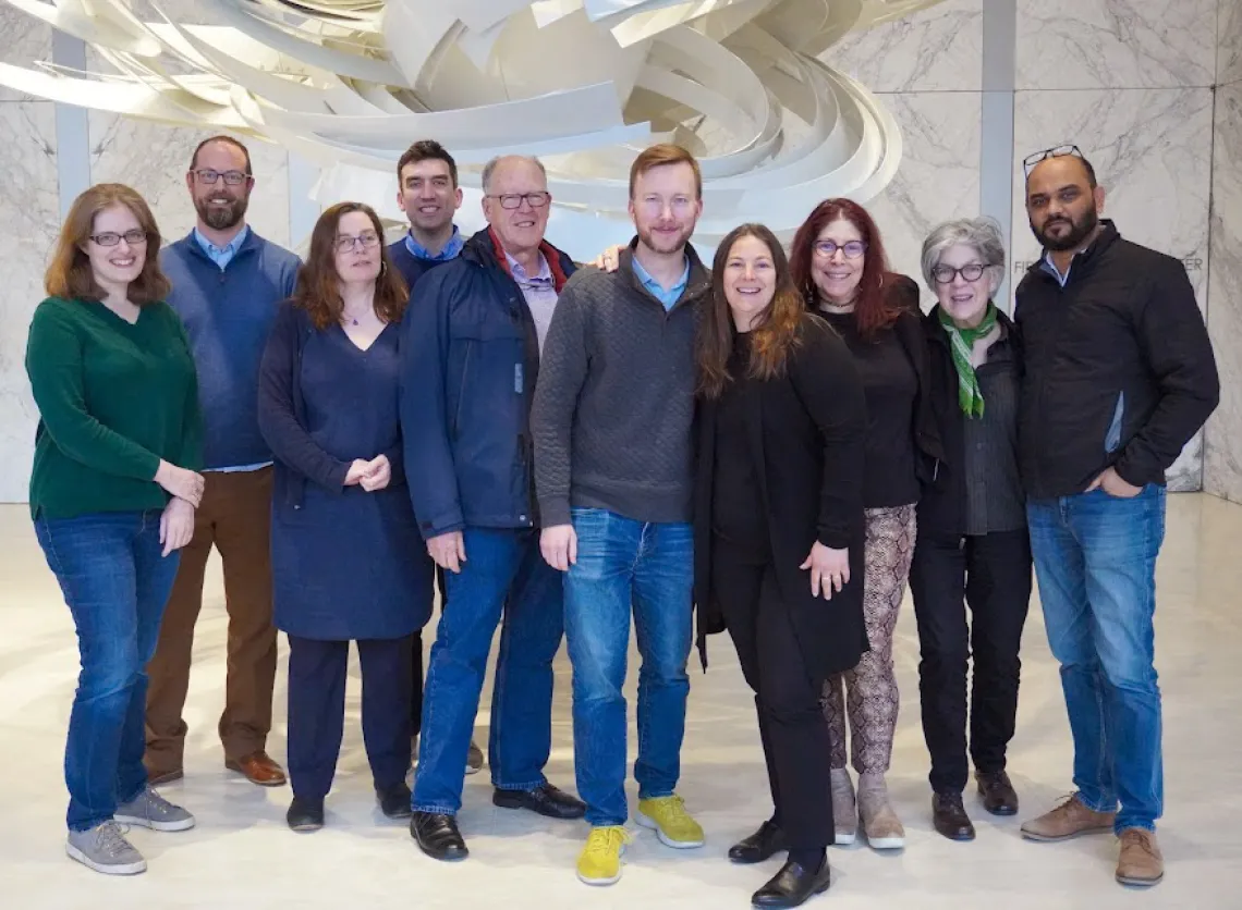 Members of the GHHIN Management Committee pose in front of a white tornadic sculpture and a gray and white marble wall.