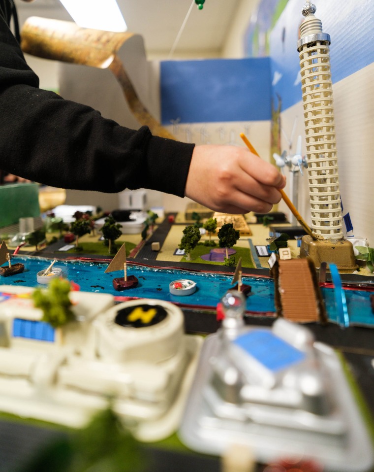 A student paints the foundation of a tower while constructing a Future City diorama.