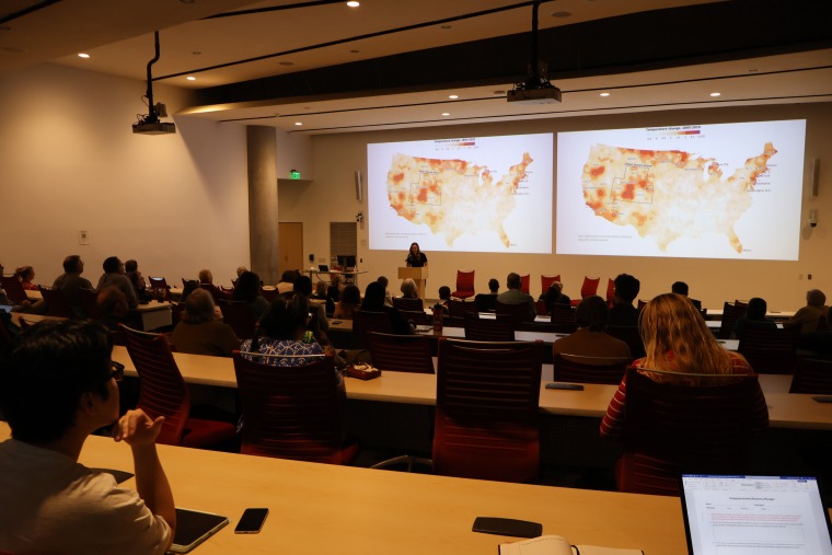 Udall Center Research Scientist Gina Gilson gives a presentation to a packed house at ENR2 during the symposium. A heat map of the US can be seen on 2 screen projected behind her.