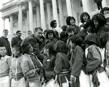 A man leaning down to shake hands with Indigenous children on the steps of the capitol building