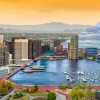 Image split diagonally with downtown Phoenix on the top left and downtown Baltimore on the bottom right.