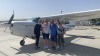 Four people pose in front of a small plane out on the tarmac.
